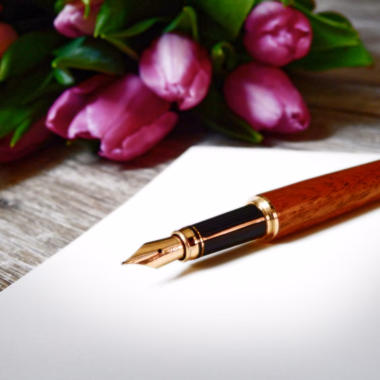 Füllfederhalter auf weißem Papier, daneben violette Tulpen
